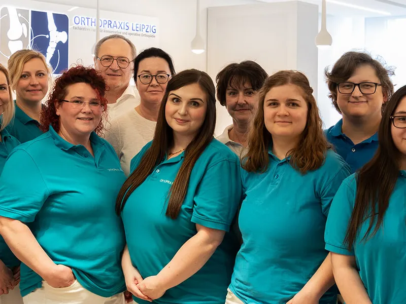 Großes Praxisteam von etwa 15 Personen in türkisfarbenen Poloshirts steht zusammen in modernen, hellen Praxisräumen