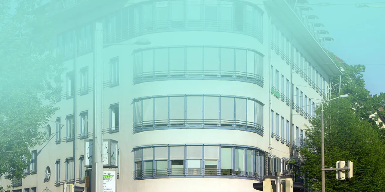 Modernes weißes Gebäude mit geschwungener Glasfassade und großen Fensterfronten in städtischer Umgebung