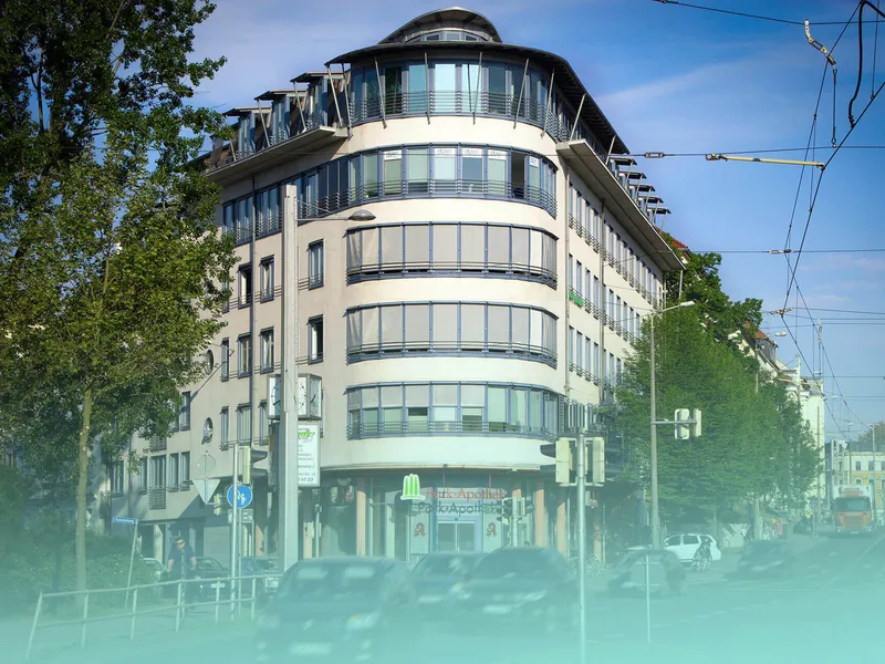 Modernes Eckgebäude mit geschwungener Glasfassade in einer begrünten Straße mit Straßenbahnlinien