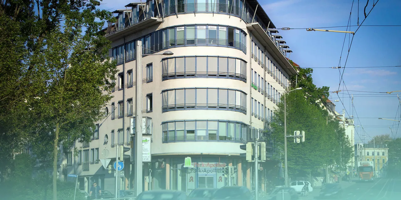 Modernes Eckgebäude mit geschwungener Glasfassade in einer begrünten Straße mit Straßenbahnlinien