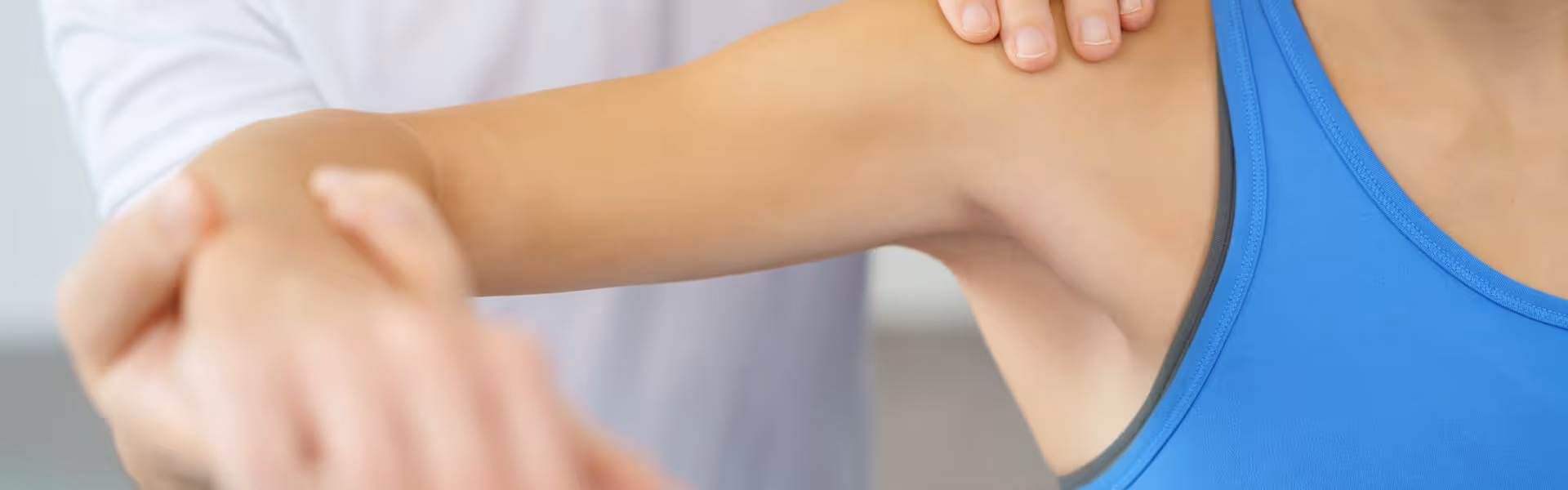 Physiotherapeut in weißem Kittel führt Armbehandlung bei Patientin in blauem Top durch