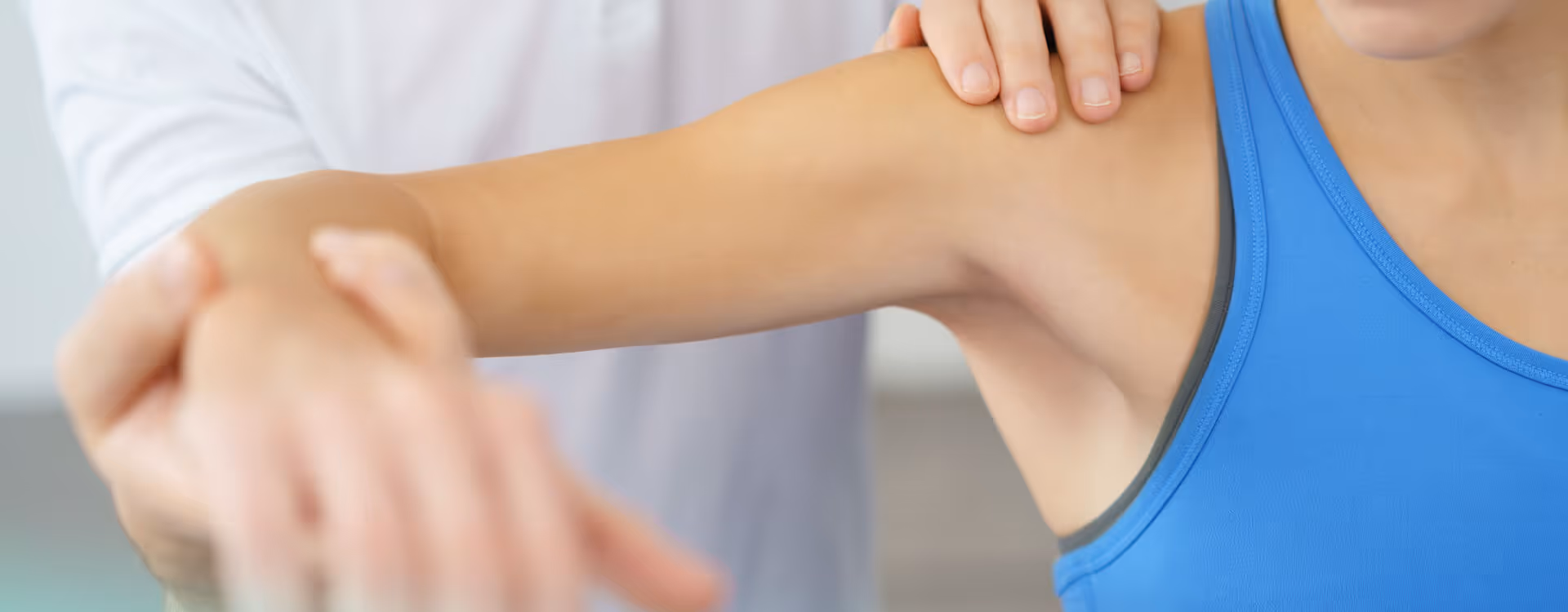 Physiotherapeut in weißem Kittel führt Armbehandlung bei Patientin in blauem Top durch