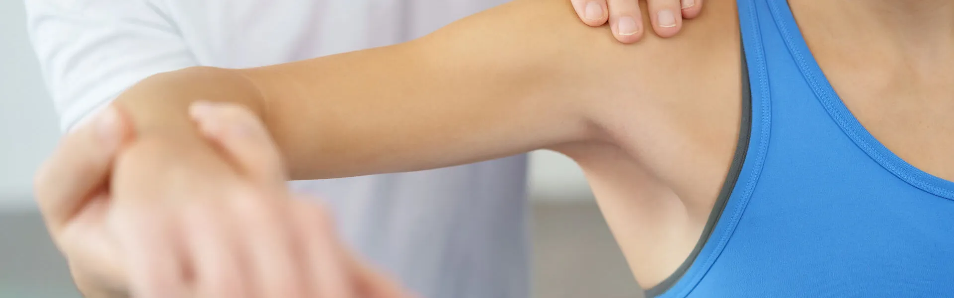 Physiotherapeut in weißem Kittel führt Armbehandlung bei Patientin in blauem Top durch