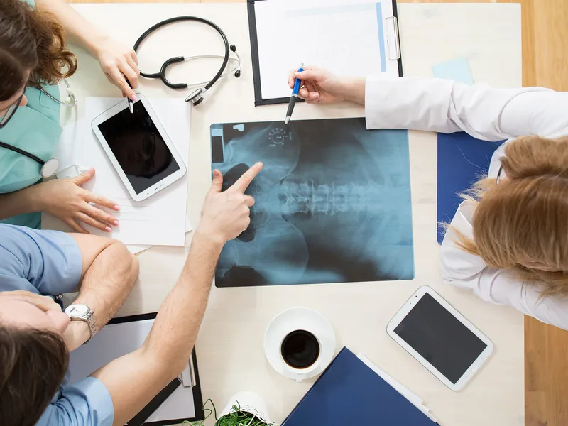 Ärzteteam bespricht Röntgenbilder am Tisch mit Tablets und Stethoskop in moderner Praxis